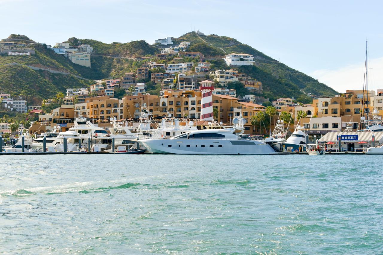 Yachts moored along the Cabo San Lucas marina waterfront beneath the hillside town