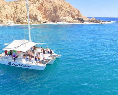 A catamaran anchored in a turquoise cove beneath desert cliffs in Los Cabos