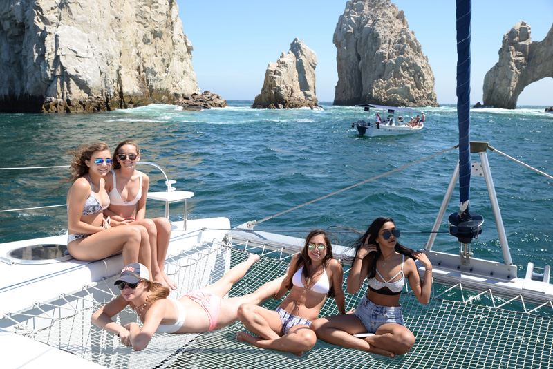 Guests relaxing on the trampoline nets of a catamaran in front of El Arco, Cabo San Lucas