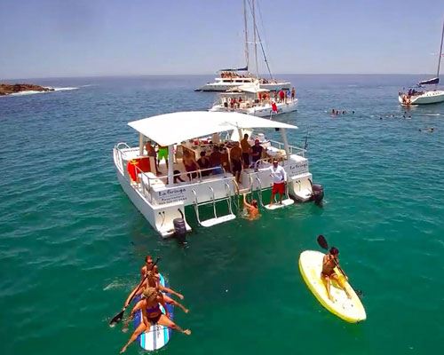 Guests paddleboarding and swimming beside an anchored catamaran in a Los Cabos bay