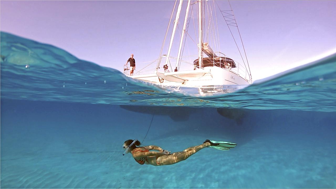 A swimmer beneath the surface beside a sailing catamaran at anchor