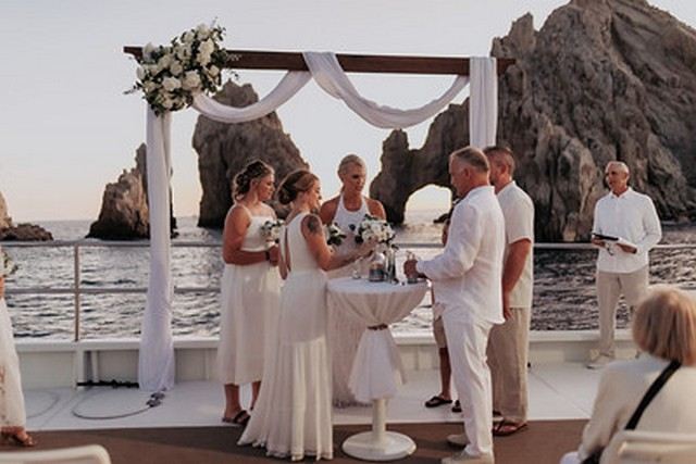 A wedding ceremony on the deck of a catamaran with the Cabo San Lucas cliffs behind