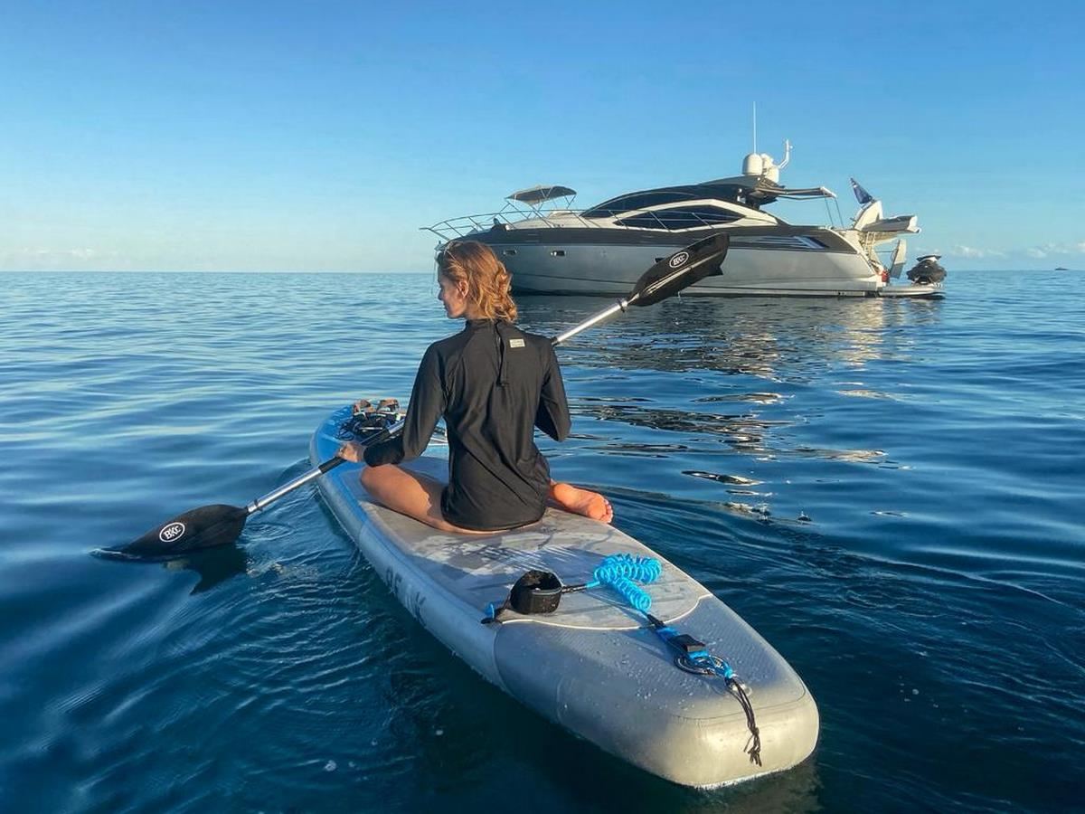 A paddleboarder setting out from an anchored sport yacht