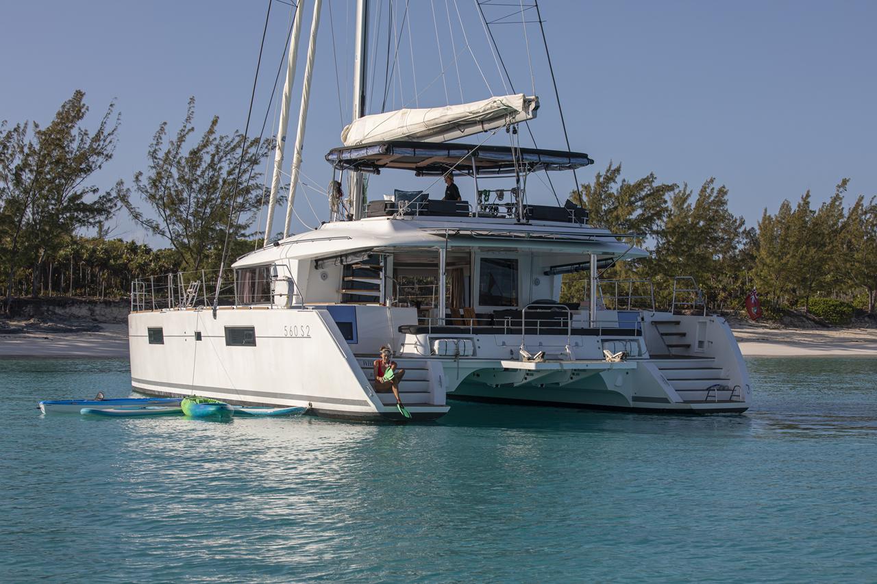 A sailing catamaran at anchor close to a tree-lined shore