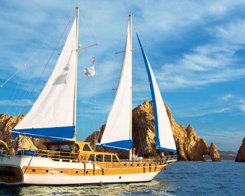 A twin-masted sailing yacht under sail near the Land's End rocks in Cabo San Lucas