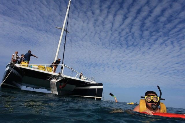 A snorkeler in the water beside a sailing catamaran