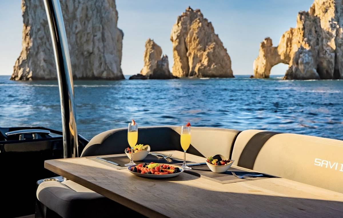 A lunch table set on a yacht's aft deck facing the Land's End arch in Cabo San Lucas